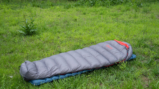 QEZER lightweight down sleeping bag laid on a sleeping pad at a grassy campsite