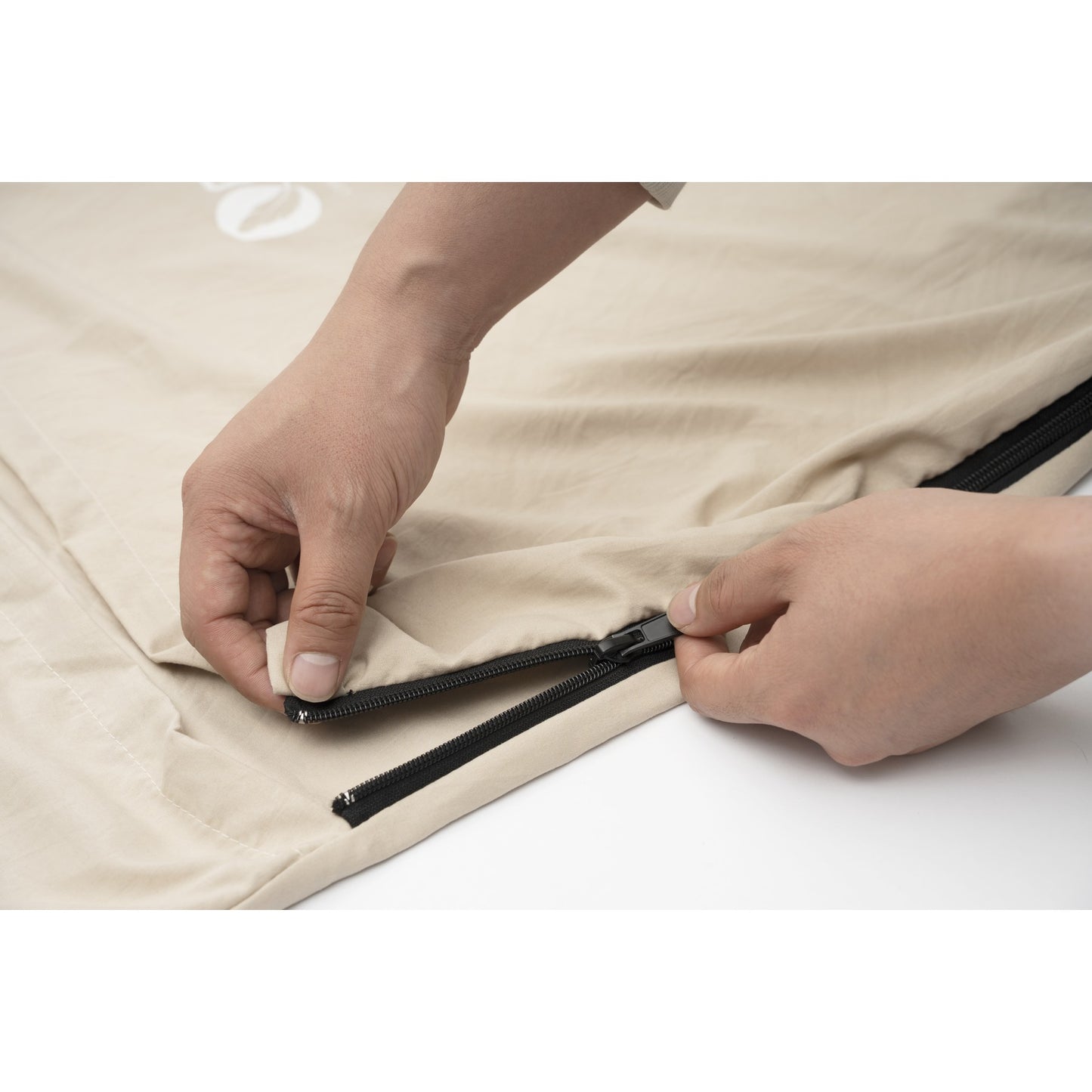 Hands closing the side zipper on a QEZER khaki sleeping bag liner